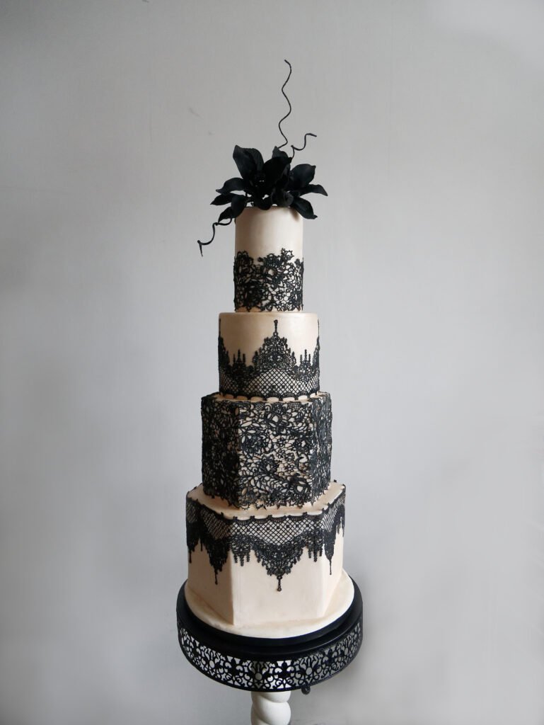 Black wedding cake with edible black lace and champagne lustre fondant icing. Black sugar lilies top this gothic chic statement piece.