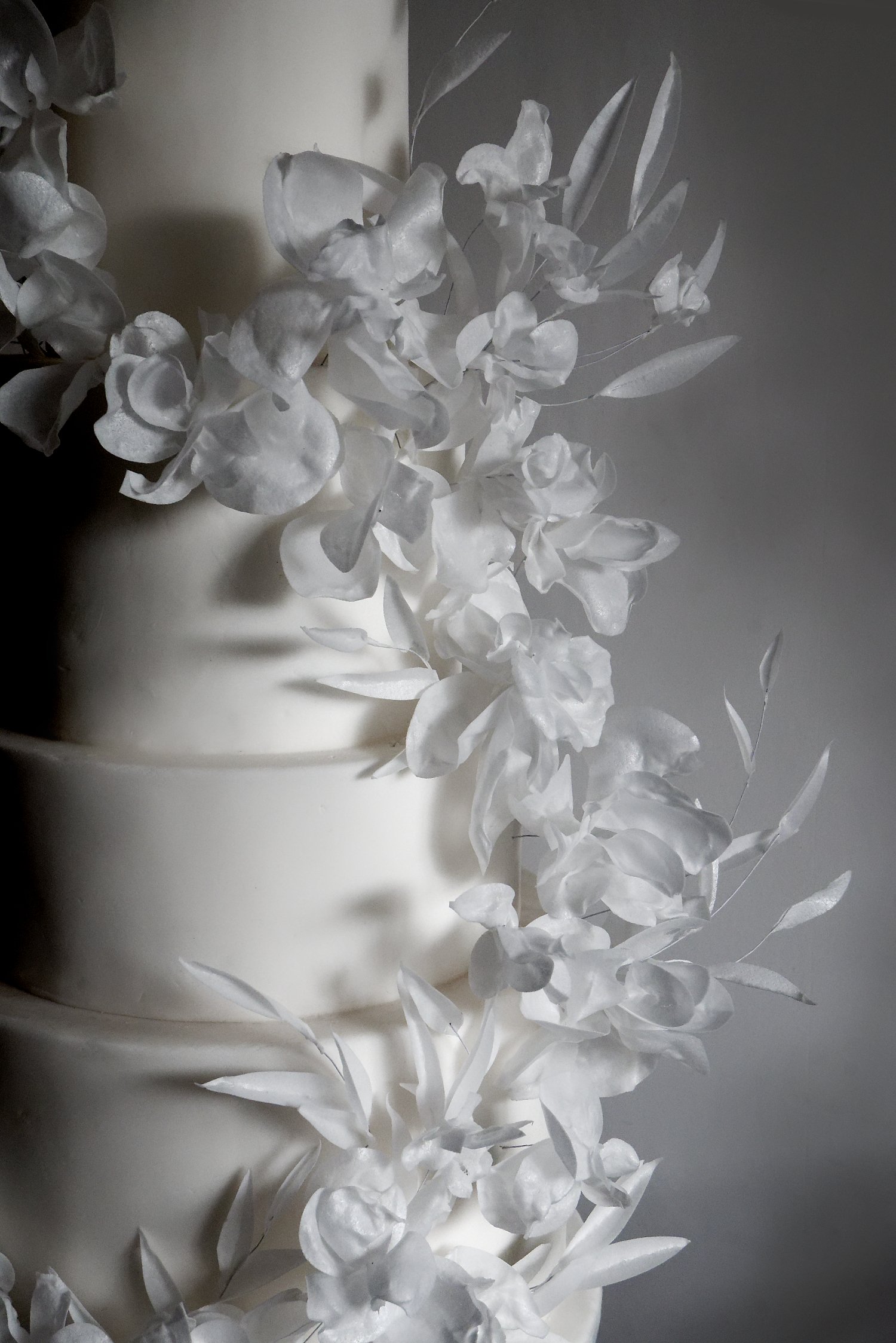 Windswept white on white ethereal wedding cake with fondant icing and wafter paper abstract flowers.